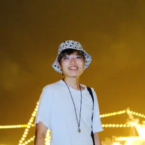 A person in a white T-shirt and patterned bucket hat smiling in front of string lights at night