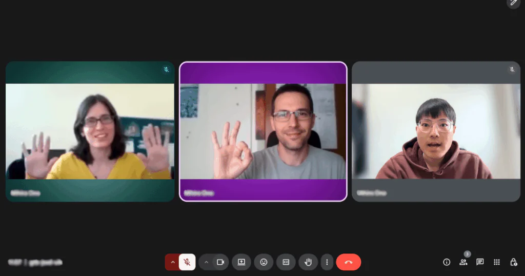 A video call with three participants waving and making an OK sign on screen