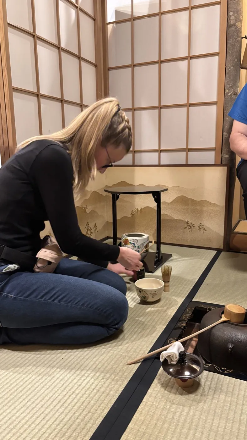 A guest whisking matcha in a tatami tea room during a tea ceremony