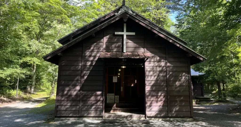 A small, dark wooden church among tall trees